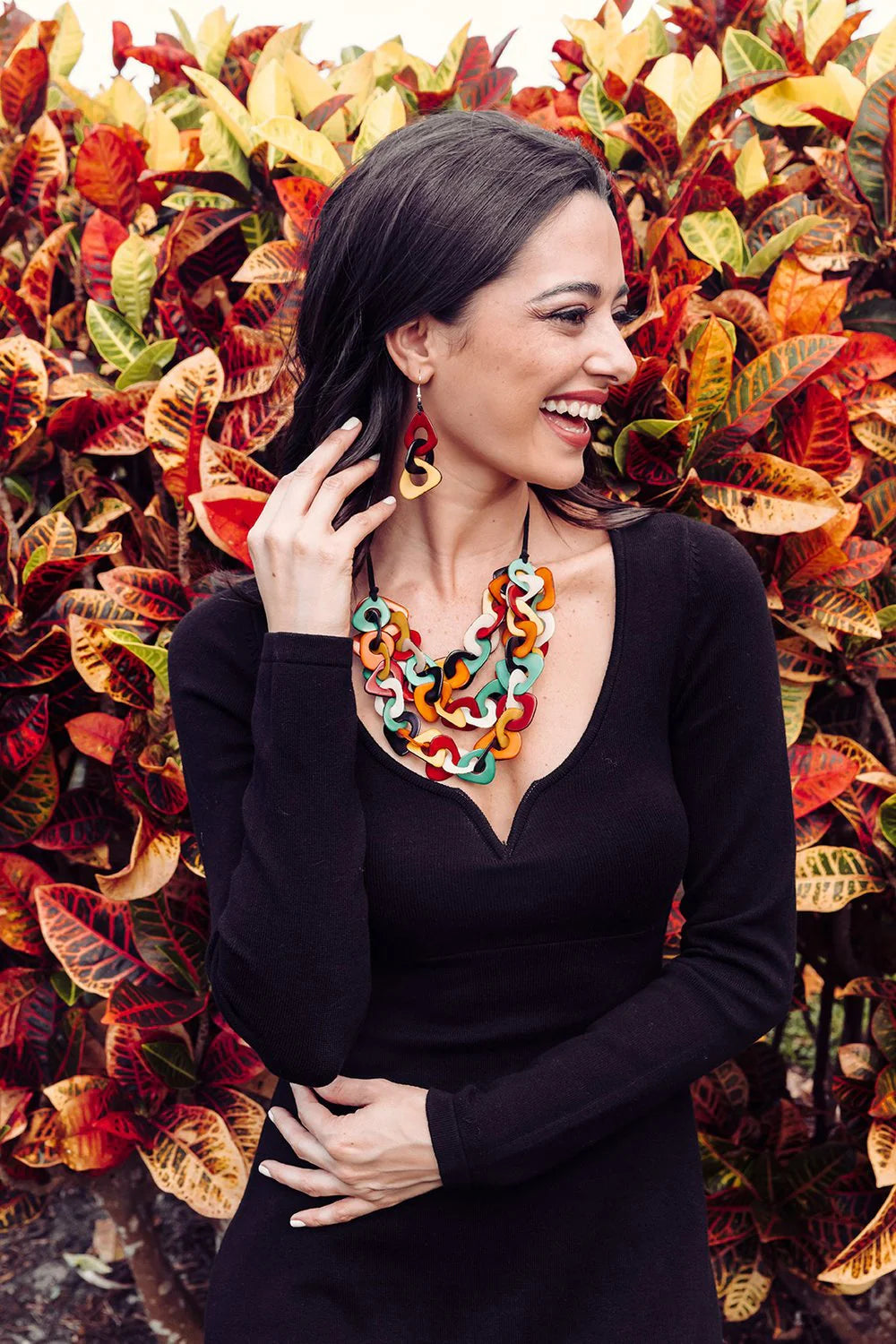 Woman wearing a colorful necklace in front of a vibrant leafy background